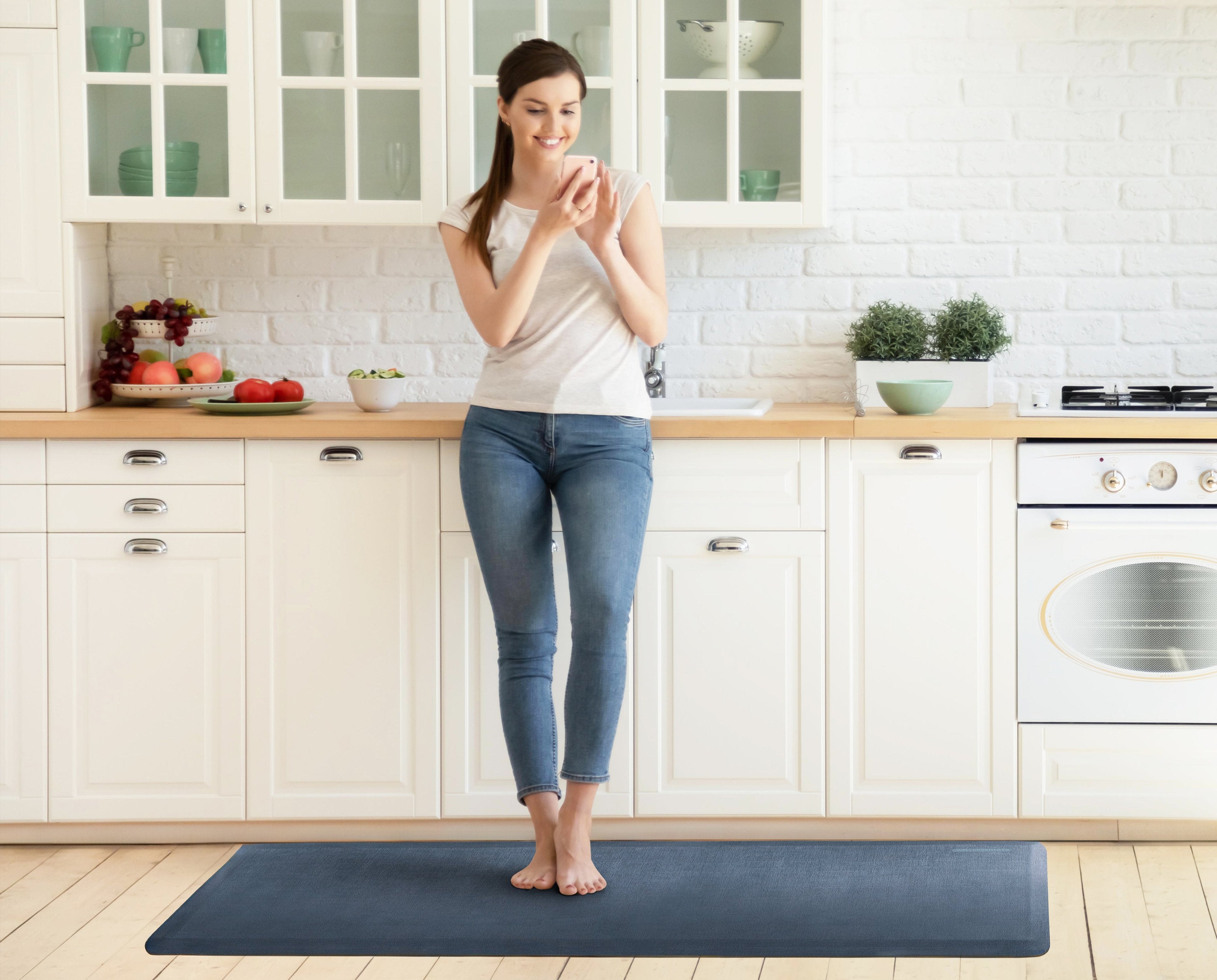 A woman standing on a 6'x2' lagoon WellnessMat in a kitchen.