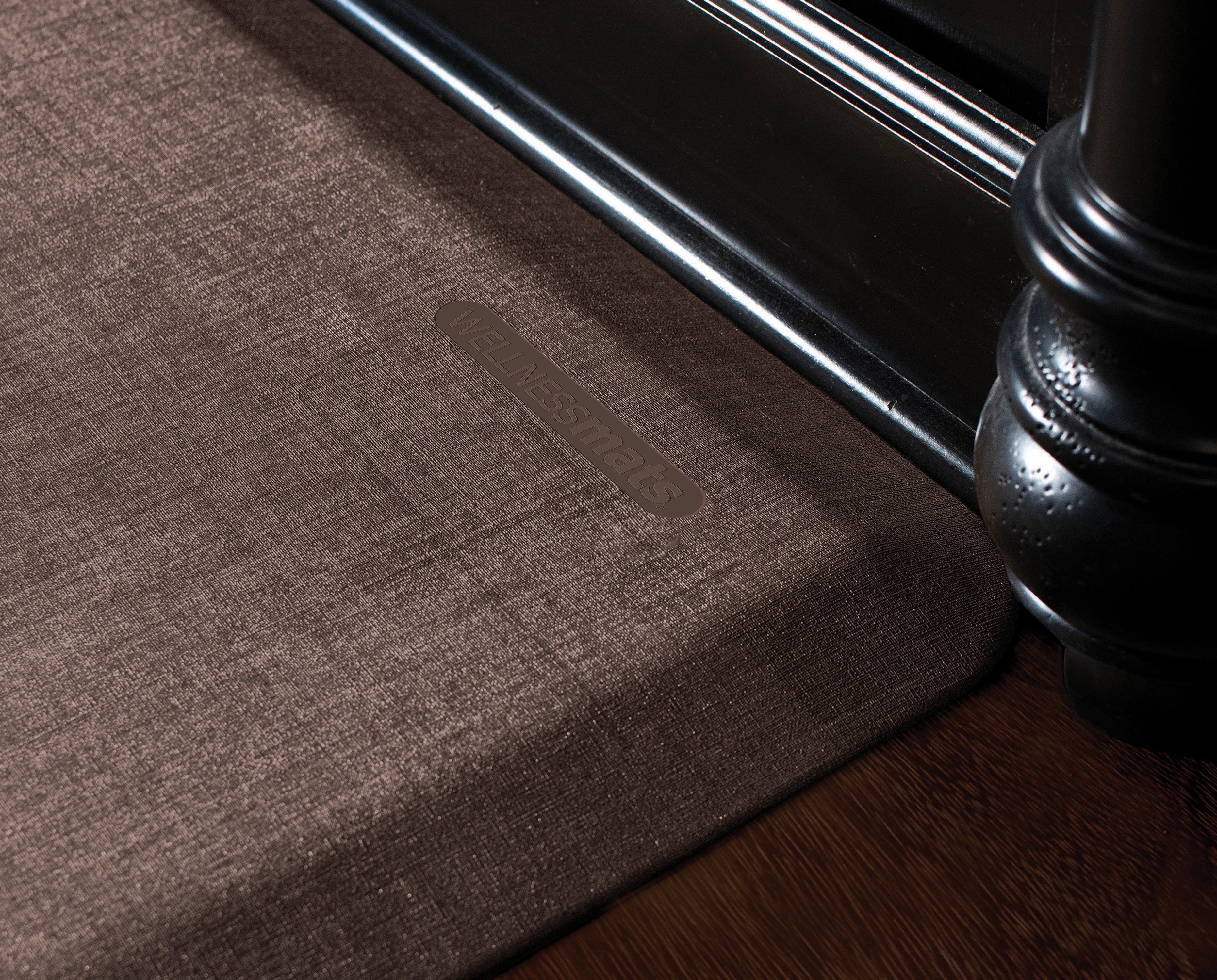 An up-close shot of a 3'x2' Antique Dark WellnessMat in front of a dark wood vanity.