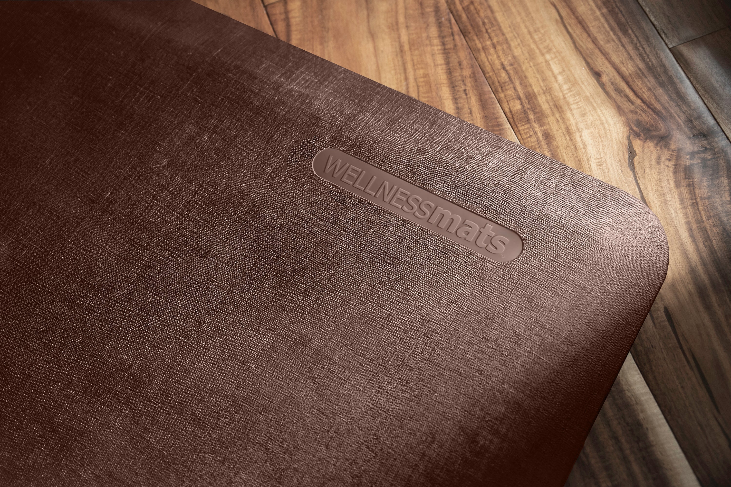 An up-close shot of a 3'x2' Antique Dark WellnessMat on a light wood floor.